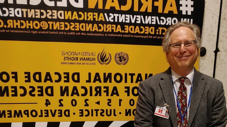 David Livert stands in front of a sign at the Permanent Forum of People of African Descent in Geneva  